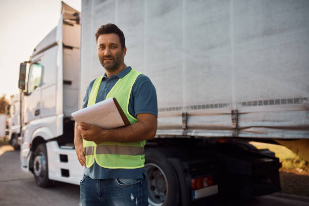 Mid adult truck dispatcher with shipment list on parking lot looking at camera.